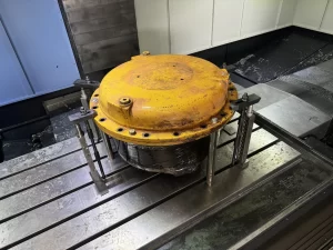 A large yellow metal cover sits on a steel workbench