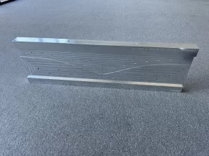 Aluminium fixture base with drill holes placed on a grey surface