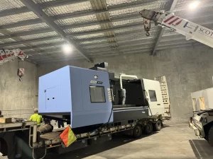 Blue and white CNC machine being unloaded indoors with crane support