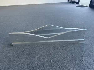 Curved aluminium component with precision holes aligned on grey carpet