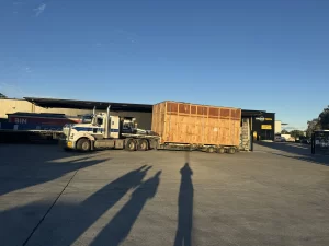 Truck parked outside warehouse with large wooden packing box