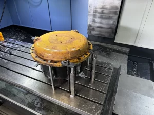 Yellow metal piece is secured by clamps on a CNC milling machine bed